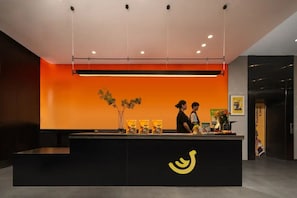 A reception desk with a black counter, a yellow logo, and two individuals standing behind it. - Banana FUN Hotel (Guangzhou Beijing Road Pedestrian Street Yuexiu Park) (Guangzhou)