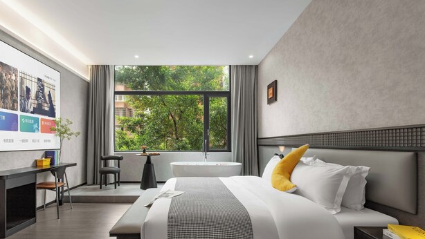 A modern hotel room with a large bed, a desk, a chair, a small table, and a large window with a view of trees. - Banana FUN Hotel (Guangzhou Beijing Road Pedestrian Street Yuexiu Park) (Guangzhou)