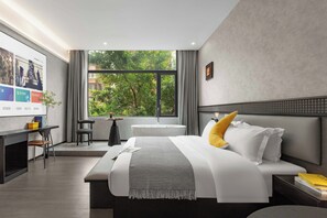 A modern hotel room with a large bed, a desk, a chair, a small table, and a large window with a view of trees. - Banana FUN Hotel (Guangzhou Beijing Road Pedestrian Street Yuexiu Park) (Guangzhou)