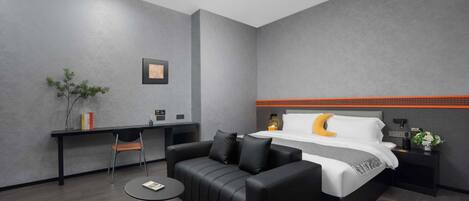 A modern hotel room with a bed, a sofa, a desk, and a small table.