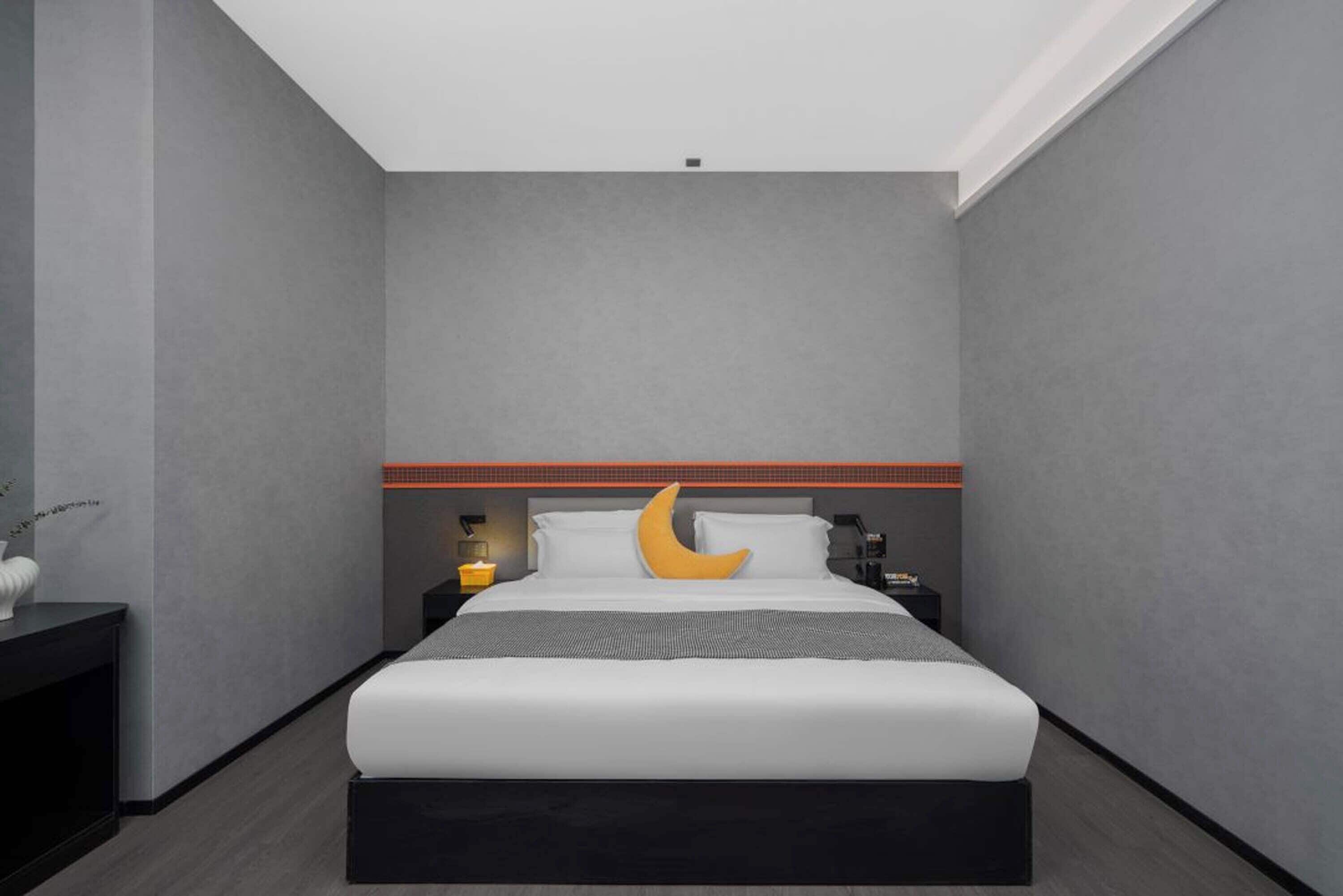 A modern hotel room with a large bed, a nightstand, a lamp, and a wall-mounted shelf.