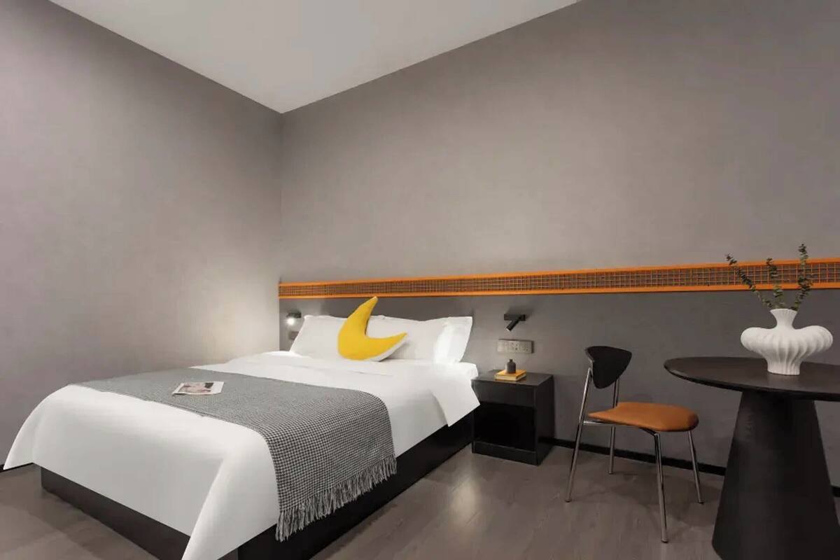 Una habitación de hotel moderna con cama, mesita de noche, silla y una pequeña mesa con un florero.