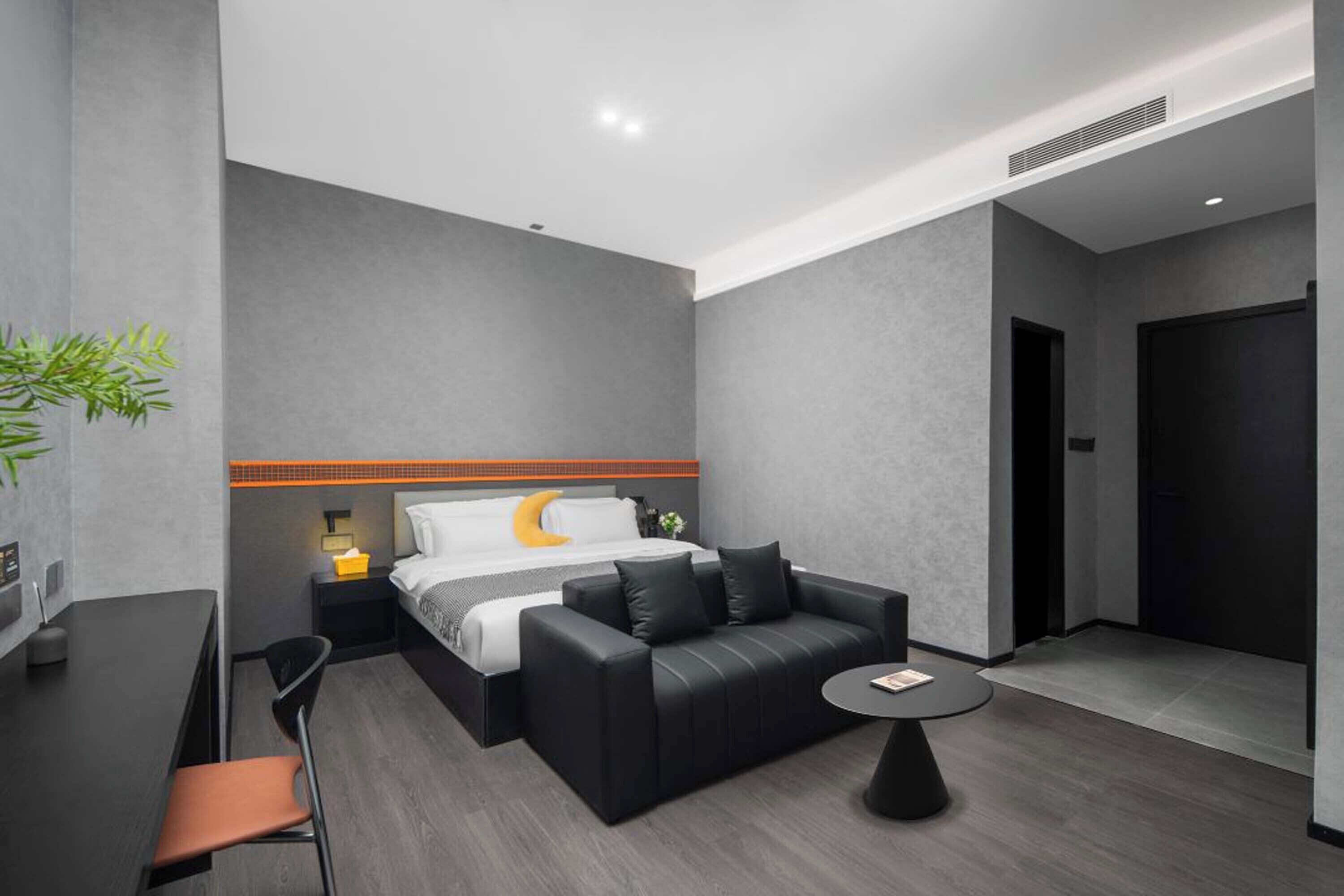 Une chambre d’hôtel moderne, équipée d’un lit, d’un canapé en cuir noir, d’une petite table ronde et d’un bureau avec une chaise.