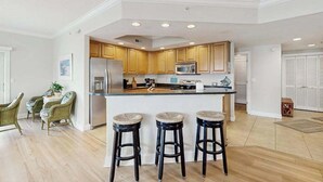 Eine moderne Küche mit Holzschränken, einem Edelstahlkühlschrank, einer Mikrowelle und einer Bar mit Hockern.