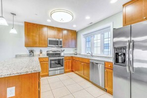 A modern kitchen with wooden cabinets, stainless steel appliances, and a large window.