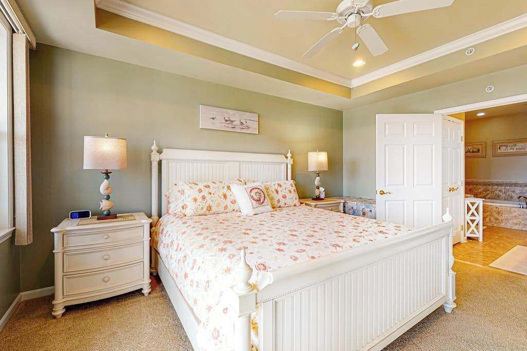 A bedroom with a bed, nightstands, a ceiling fan, and a door leading to another room.