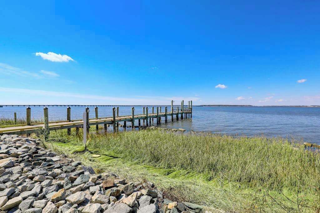 Un muelle de madera se adentra en aguas tranquilas, rodeado de zonas verdes y un litoral rocoso.