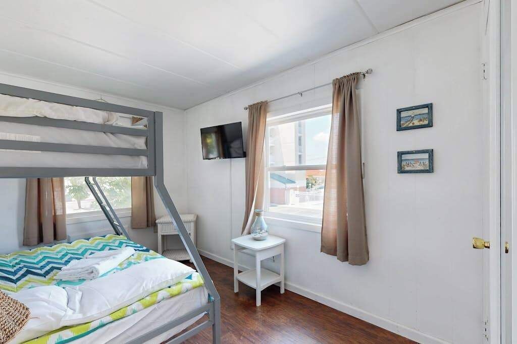 Een kamer met een stapelbed, een bureau, een stoel, een televisie en een raam met gordijnen.