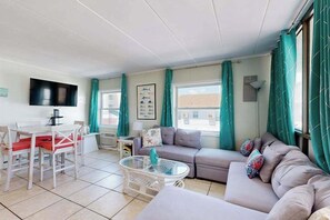 A living room with a sofa, a coffee table, a TV, and a dining area with chairs and a table. - Renovated Sherwood West Condo | Balcony & 4 Flat-Screen TVs | 400’ to Beach (Ocean City)