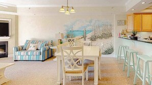 A living room with a sofa, dining table, chairs, and a kitchen area with wooden cabinets. - Midtown Condo with Balcony, Gas Fireplace, Washer/Dryer, WiFi & Shared Pool (Ocean City)
