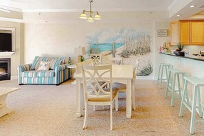 A living room with a sofa, dining table, chairs, and a kitchen area with wooden cabinets. - Midtown Condo with Balcony, Gas Fireplace, Washer/Dryer, WiFi & Shared Pool (Ocean City)