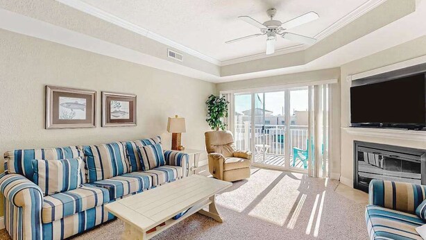 A living room with a sofa, armchair, TV, fireplace, and a balcony with a view. - Midtown Condo with Balcony, Gas Fireplace, Washer/Dryer, WiFi & Shared Pool (Ocean City)