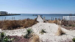 A sandy beach path leading to a pier extending into calm waters, with sparse vegetation and a clear sky. - Midtown Condo with Balcony, Gas Fireplace, Washer/Dryer, WiFi & Shared Pool (Ocean City)