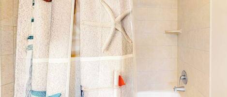 Un baño con bañera, ducha y cortina decorada con motivos playeros.
