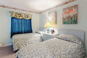 A bedroom with two beds, a nightstand, a lamp, and floral artwork on the wall. - Sunchaser 305 (Ocean City)