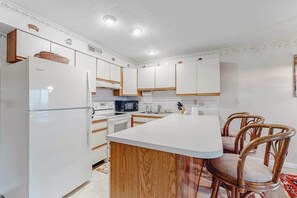 A modern kitchen with white cabinets, a central island, and wooden chairs. - Sunchaser 305 (Ocean City)