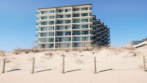 Hotel de vários andares com varandas, situado numa praia de areia.