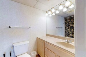 A bathroom with a toilet, a sink, a mirror, and a towel rack. - Oceanfront Condo with Balcony, Central AC, Washer/Dryer, WiFi & Shared Pool (Ocean City)