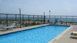 Piscina com vista para a praia, cercada por cadeiras de descanso.