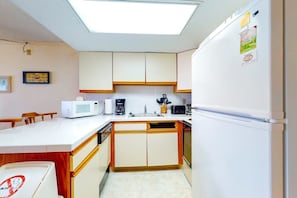 Eine kleine Küche mit weißen Schränken, einer Mikrowelle, einer Kaffeemaschine und einem Kühlschrank.