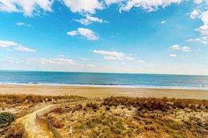 Ein Strand mit einem Weg zum Wasser, einem Zaun und einem klaren Himmel.