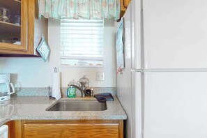 A kitchen with a granite countertop, stainless steel sink, and a white refrigerator. - Bayfront Condo with Bay/Wetland Views, Balcony, WiFi & AC - Walk to the Beach (Ocean City)