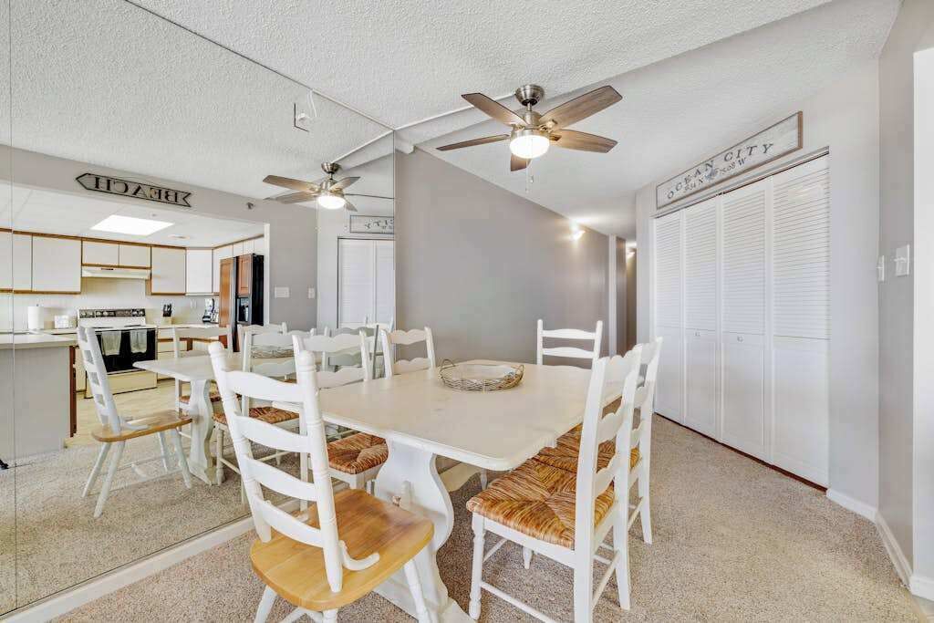 A dining area with a white table and chairs, ceiling fans, and a kitchen in the background.