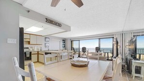 Eine moderne Küche mit weißen Schränken, ein Essbereich mit großem Tisch und Stühlen sowie Meerblick durch große Fenster.