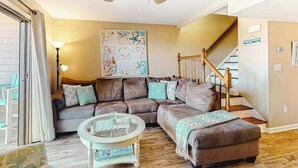 Ein Wohnzimmer mit Ecksofa, einem Glastisch, einer Treppe mit Holzbalken und einem Deckenventilator.