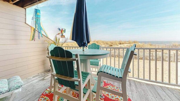 Ein überdachter Außenbereich mit Tisch und Stühlen, einem Sonnenschirm und Blick auf den Strand.