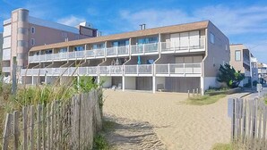 Ein mehrstöckiges Hotel mit Balkonen, einem Sandstrand davor und einem Holzzaun.