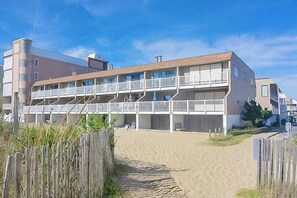 Ein mehrstöckiges Hotel mit Balkonen, einem Sandstrand davor und einem Holzzaun.