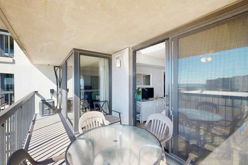 A balcony with a glass table and chairs, a white dresser, and a TV in the background.