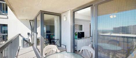 A balcony with a glass table and chairs, a white dresser, and a TV in the background.