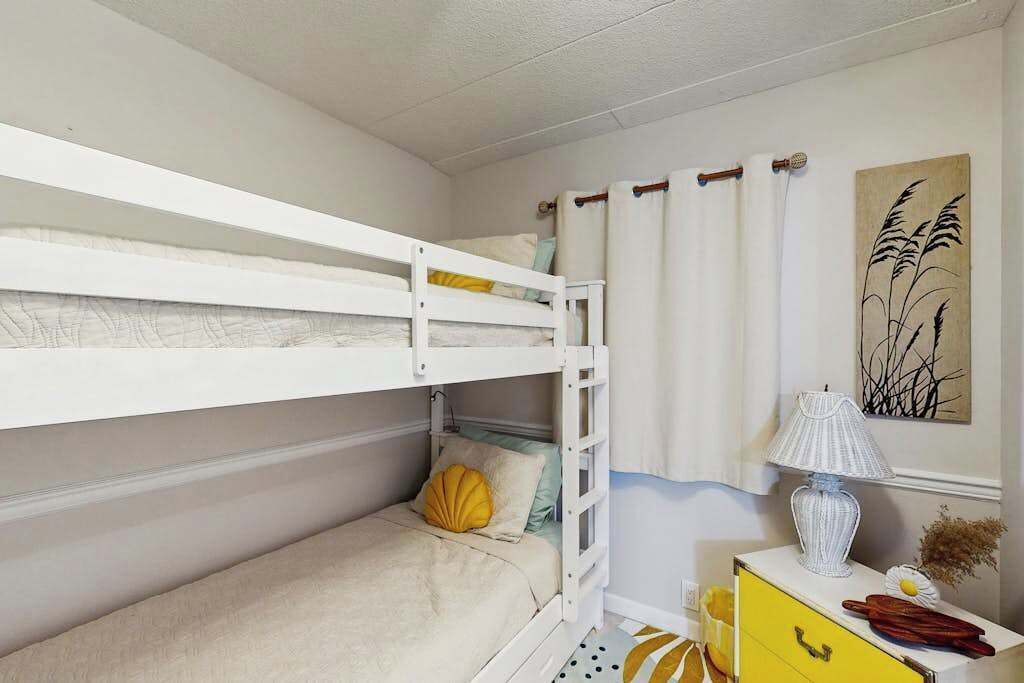 Quarto com beliche, uma pequena mesa, um abajur e um quadro na parede.