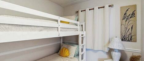 Quarto com beliche, uma pequena mesa, um abajur e um quadro na parede.