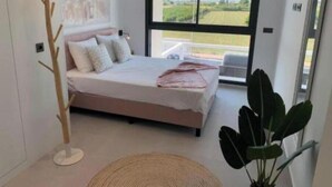 A bedroom with a bed, a large window, a plant, and a floor lamp. - Flamenco House (Rojales)