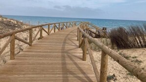 A wooden boardwalk leading to the beach with a sandy landscape and ocean in the background. - Flamenco House (Rojales)
