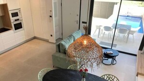 A modern kitchen with built-in appliances, a dining area with a round table and chairs, and a view of an outdoor pool area. - Flamenco House (Rojales)