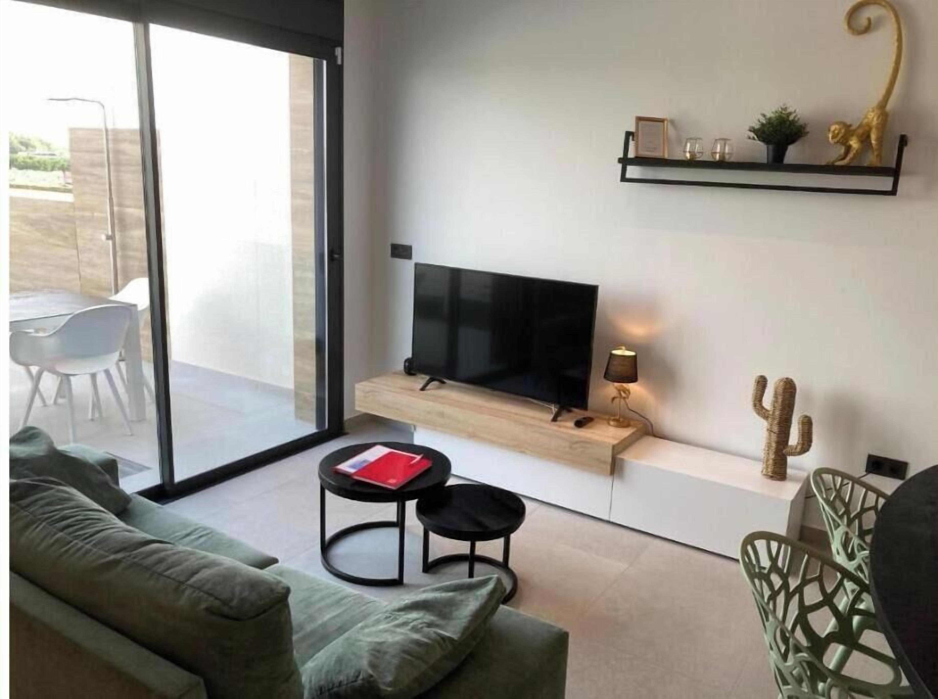 Ett modernt vardagsrum med en platt-TV, en soffa, ett soffbord och en kaktus på en hylla.
