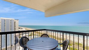 Ein Balkon mit Tisch und Stühlen mit Blick auf Strand und Meer.
