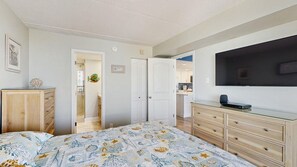 A bedroom with a bed, a dresser, a TV, and a door leading to another room. - Stunning beachfront condo with balcony, pools, game room, sauna & gym (Ocean City)