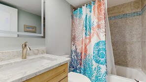A bathroom with a shower curtain, a sink, a mirror, and a bathtub. - Stunning beachfront condo with balcony, pools, game room, sauna & gym (Ocean City)