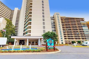 A hotel with a large building, a sign for 'Sea Watch,' and a parking lot. - Modern & affordable beach condo with pools, gym, tennis, sauna & central AC (Ocean City)