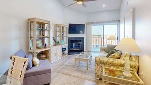 Un salón con sofá, sillón, mesa de centro, estantería, chimenea y vistas al balcón.