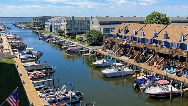 Un puerto deportivo con barcos amarrados, un muelle de madera y una hilera de edificios con balcones.