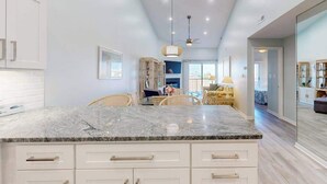 Una cocina moderna con una isla de mármol, armarios blancos e iluminación colgante.