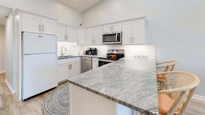 Una cocina moderna con armarios blancos, encimera de granito, refrigerador, microondas y estufa.