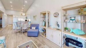 Amplia sala de estar con una mesa de comedor, un sofá azul y una estantería con objetos decorativos.