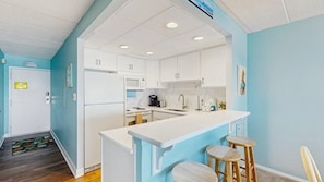 A kitchen with white cabinets, a microwave, a sink, and a bar area with stools. - Stunning Beachfront Condo- fully equipped w/Shared Pool & Private Balcony & WiFi (Ocean City)
